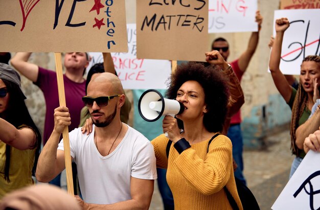 Mujer afroamericana gritando por megáfono mientras marcha con un grupo de personas en una protesta por los derechos humanos