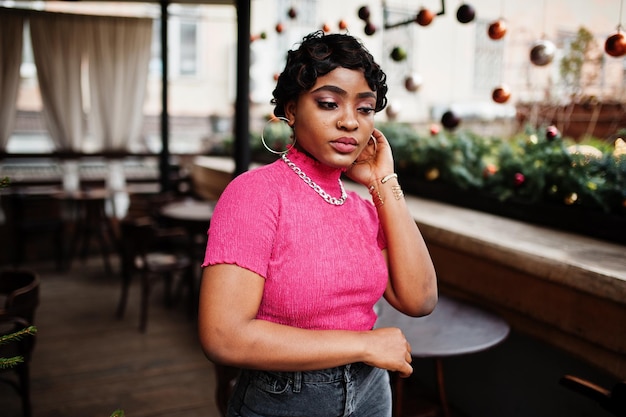 Mujer afroamericana joven urbana en top rosa y jeans grises Mujeres chic de moda afro con piercing de anillo en la nariz