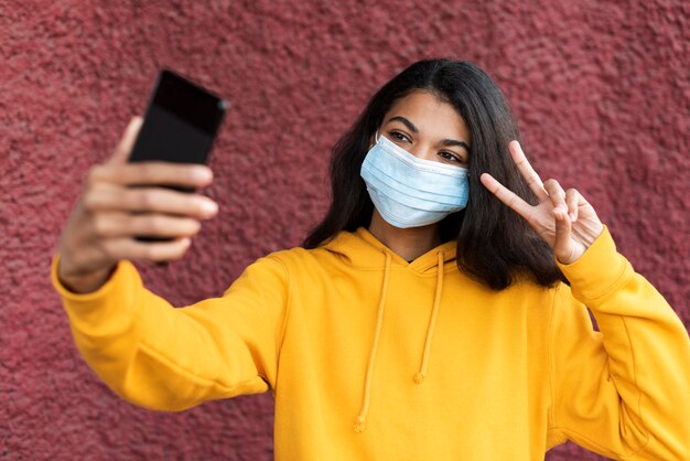 Mujer afroamericana con una máscara médica y tomando un selfie