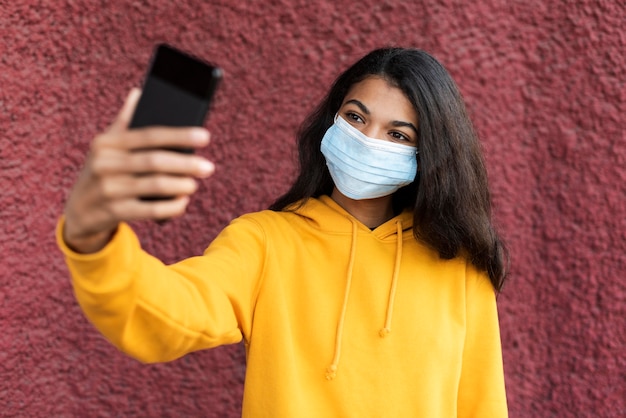 Mujer afroamericana con una máscara médica y tomando un selfie