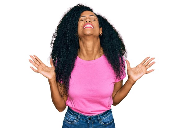 Mujer afroamericana de mediana edad con ropa informal celebrando loca y loca por el éxito con los brazos levantados y los ojos cerrados gritando emocionada. concepto de ganador