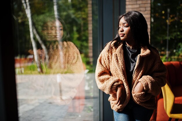 Mujer afroamericana de moda usa chaqueta de pie cerca de la ventana
