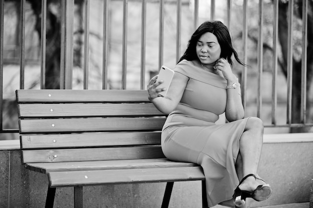 Mujer afroamericana modelo xxl en vestido naranja mirando en el teléfono móvil