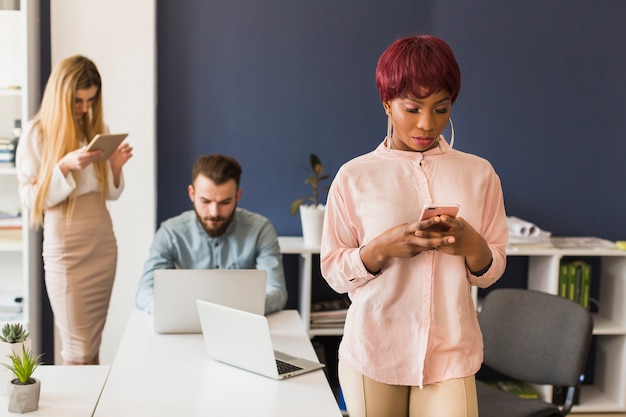 Mujer afroamericana, navegación, teléfono inteligente, en la oficina