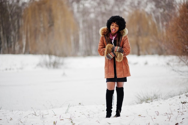 Mujer afroamericana de pelo rizado vestida con abrigo de piel de oveja y guantes posados en el día de invierno muestra que hace frío