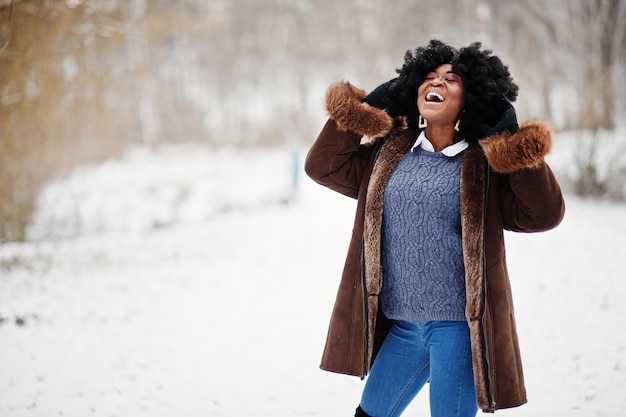 Mujer afroamericana de pelo rizado vestida con abrigo de piel de oveja y guantes posados en el día de invierno