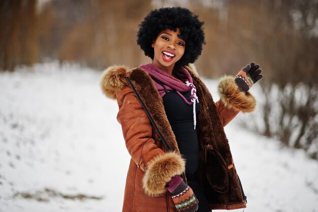 Mujer afroamericana de pelo rizado vestida con abrigo de piel de oveja y guantes posados en el día de invierno
