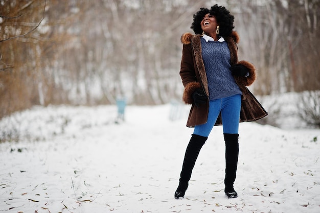 Mujer afroamericana de pelo rizado vestida con abrigo de piel de oveja y guantes posados en el día de invierno