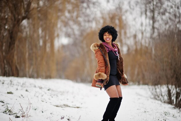 Mujer afroamericana de pelo rizado vestida con abrigo de piel de oveja y guantes posados en el día de invierno