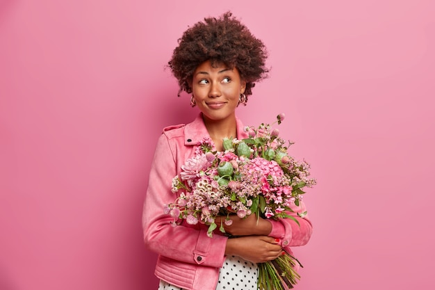 Mujer afroamericana pensativa con hermoso ramo de flores, vestida con ropa de moda,