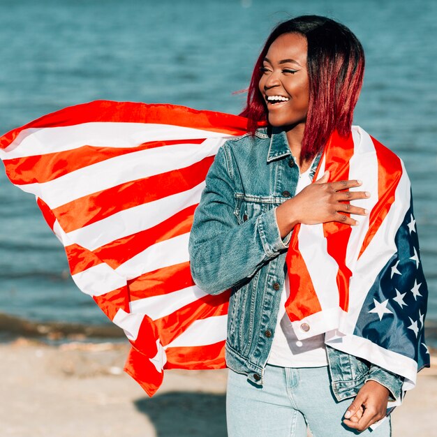 Mujer afroamericana de pie con bandera americana en el hombro
