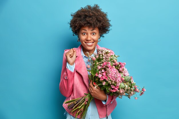 La mujer afroamericana positiva aprieta los puños celebra la obtención de flores en el Día Internacional de la Mujer posa con ramo