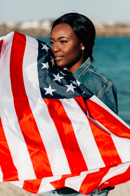 Mujer afroamericana que sostiene la bandera americana que se inclina contra la cara