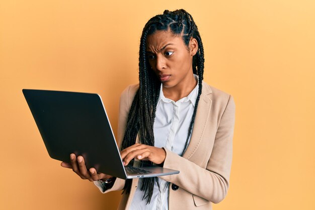 Mujer afroamericana que trabaja usando computadora portátil escéptica y nerviosa, frunciendo el ceño molesta por el problema. persona negativa