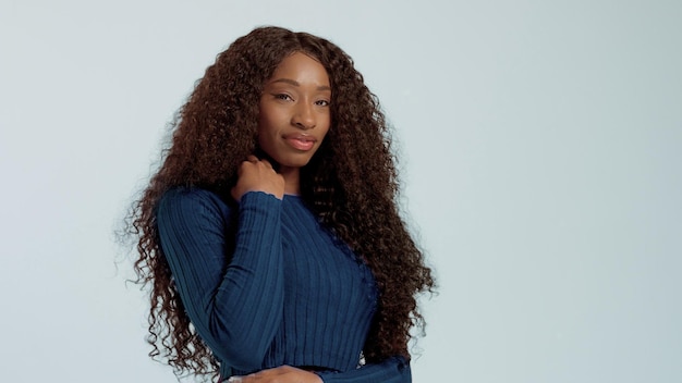 Mujer afroamericana de raza mixta negra de belleza con cabello largo y rizado y sonrisa perfecta mirando a la cámara y sonriendo en azul