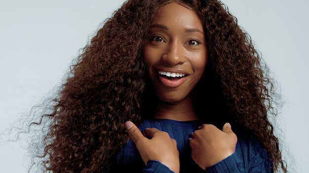 Mujer afroamericana de raza mixta negra de belleza con cabello largo y rizado y una sonrisa perfecta mirando a la cámara y sonriendo y preguntándose y sorprendida