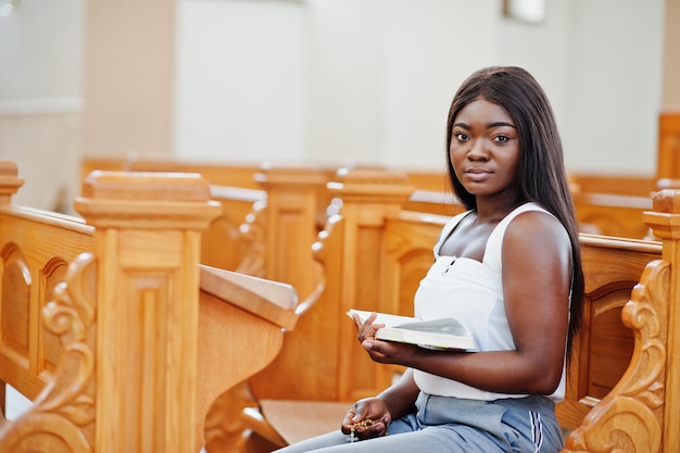 Mujer afroamericana rezando en la iglesia Los creyentes meditan en la catedral y el tiempo espiritual de oración Niña afro sostiene rosario y biblia mientras está sentada en un banco