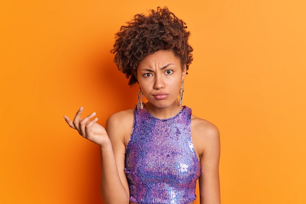 Foto gratuita la mujer afroamericana rizada descontenta descontentada tiene expresión confusa despistada levanta la mano y mira dudosa