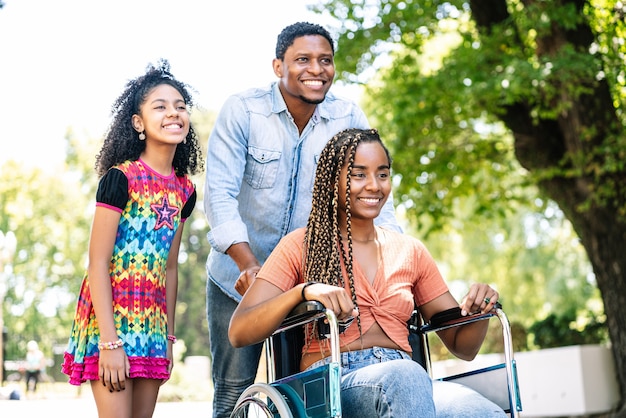 Una mujer afroamericana en silla de ruedas disfrutando de un paseo al aire libre con su hija y su marido.