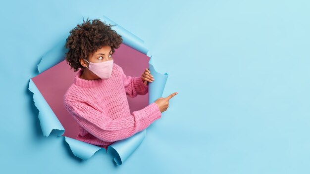 Mujer afroamericana sorprendida se para de lado y apunta hacia un espacio vacío