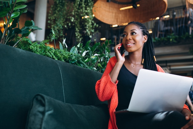 Mujer afroamericana con teléfono y computadora portátil en un café