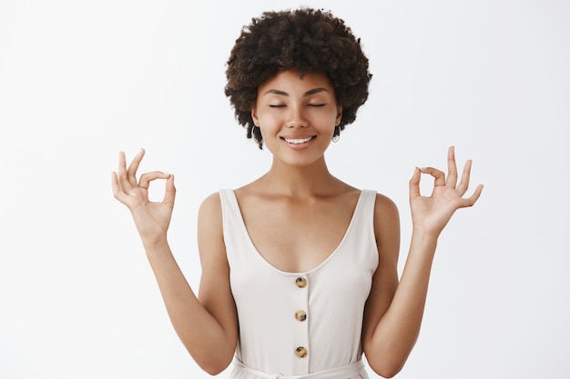 Mujer afroamericana tranquila y relajada, feliz, aliviada y con ropa de moda, cerrando los ojos y sonriendo, tomados de la mano levantados con gesto zen, meditando