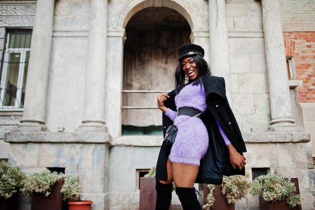 Mujer afroamericana en vestido violeta y gorra posada al aire libre