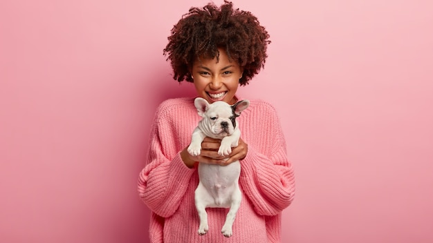 Mujer afroamericana vistiendo suéter rosa con cachorro