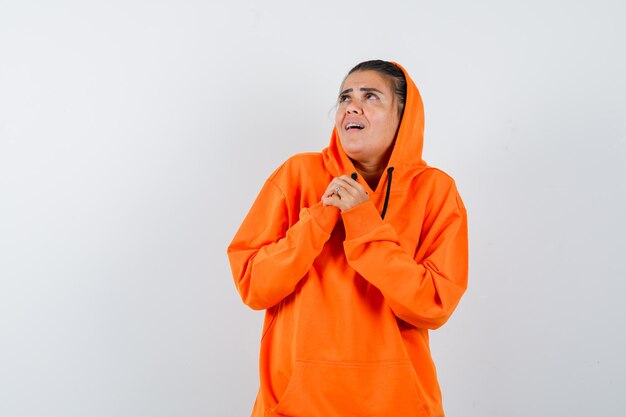 Mujer agarrando las manos sobre el pecho en sudadera con capucha naranja y mirando avergonzado