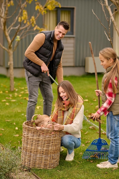 Mujer agazapada admirando niño en cesta hombre y niña limpieza