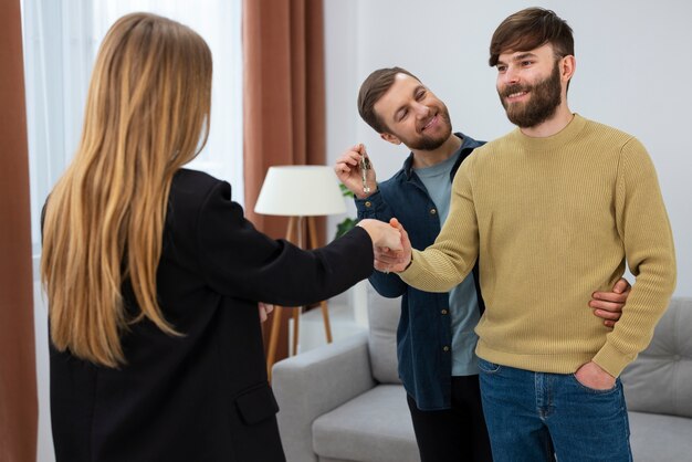 Mujer agente de bienes raíces hablando de negocios y mostrando la casa a una pareja gay