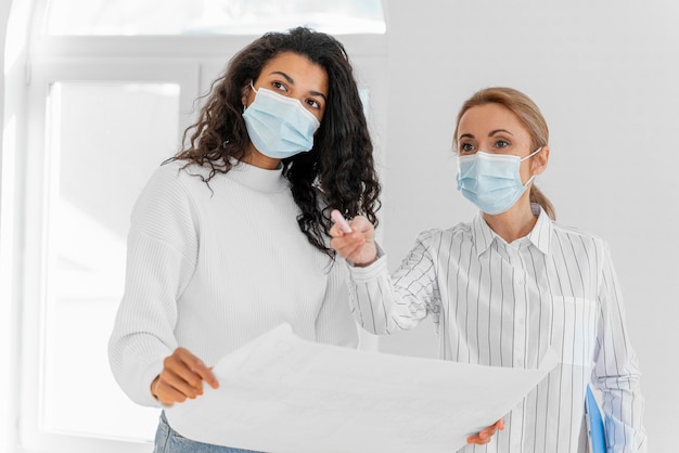 Foto gratuita mujer y agente de bienes raíces con planes de casa juntos con máscaras médicas