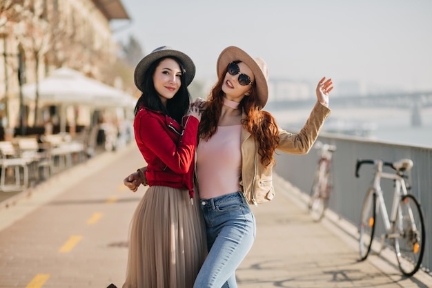 Mujer agraciada en jeans azul bailando mientras posa con su hermana morena