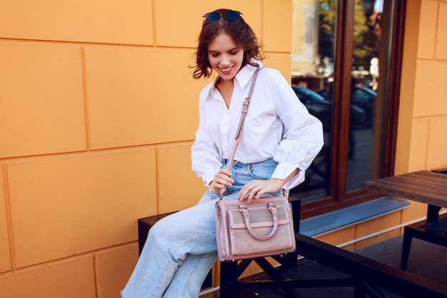 Foto gratuita mujer agraciada en traje casual sentado cerca de café moderno con paredes amarillas. look de moda. humor positivo.