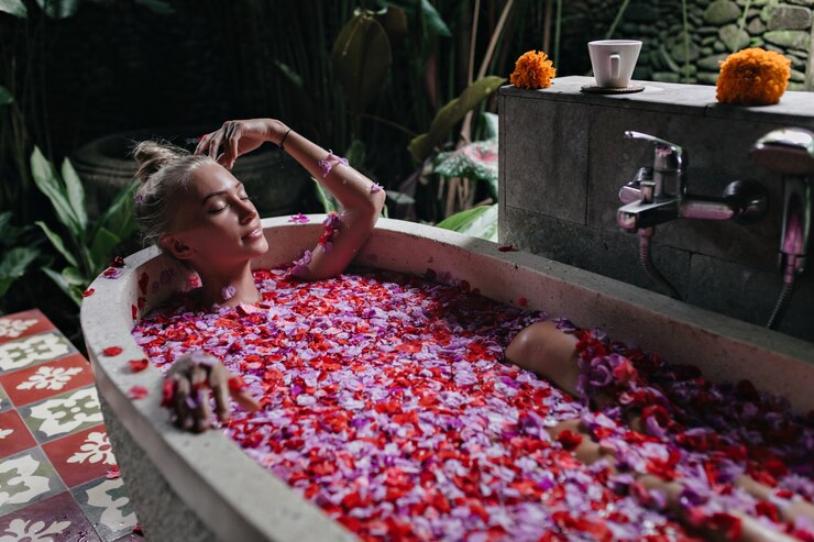 Mujer agradable con piel bronceada tumbada en el baño con los ojos cerrados. Filmación en interiores de linda dama rubia disfrutando de spa con pétalos de rosa.
