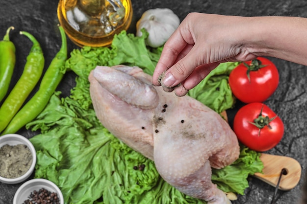 La mujer agrega especias al pollo crudo con un montón de verduras.