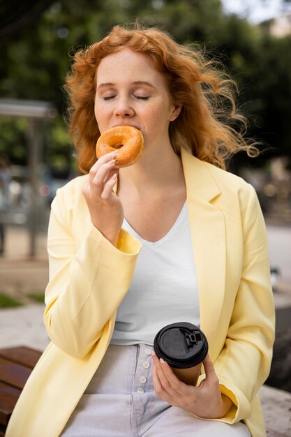 Mujer al aire libre disfrutando de una deliciosa dona y una taza de café