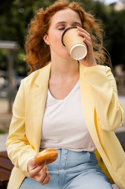 Mujer al aire libre disfrutando de una deliciosa dona y una taza de café