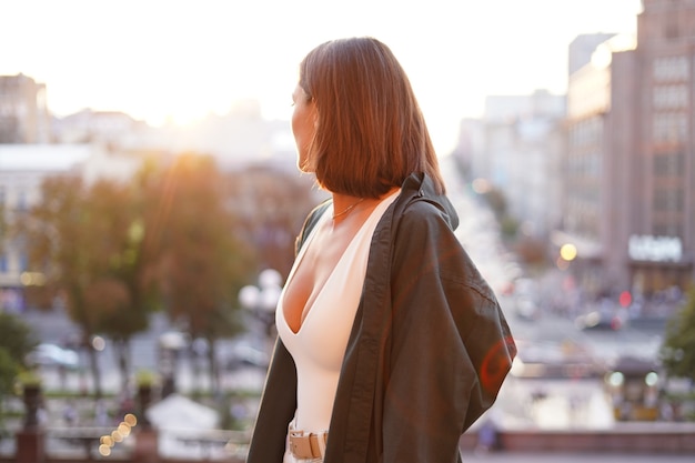 Mujer al atardecer con increíbles vistas a la ciudad, disfrutando de días cálidos, libertad, vibraciones positivas