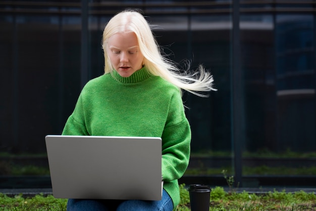 Mujer albina de tiro medio que trabaja con una computadora portátil