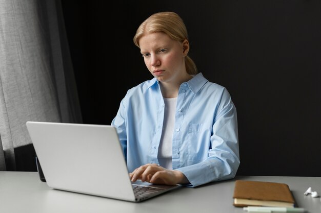 Mujer albina de tiro medio trabajando en una computadora portátil