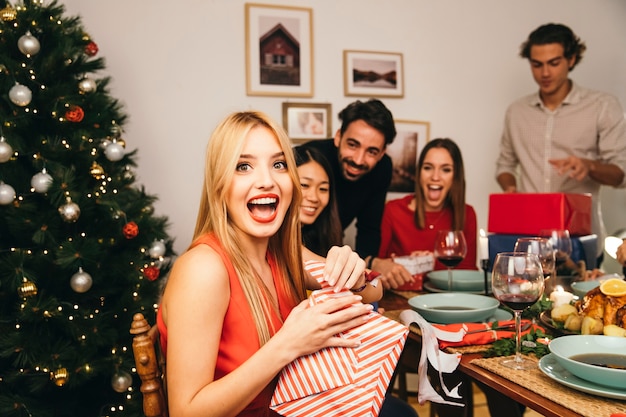 Mujer alegre abriendo regalo en cena de navidad