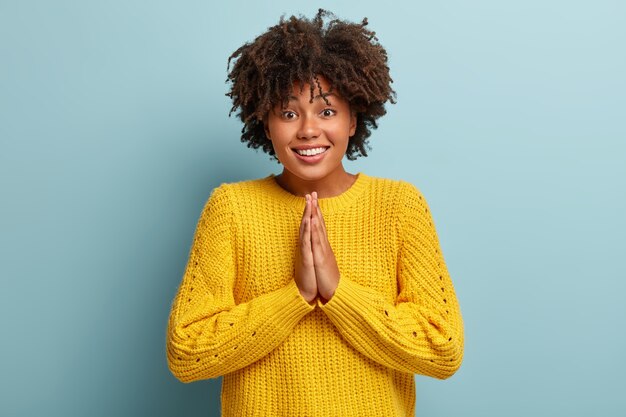 Mujer alegre con un afro posando en un suéter rosa