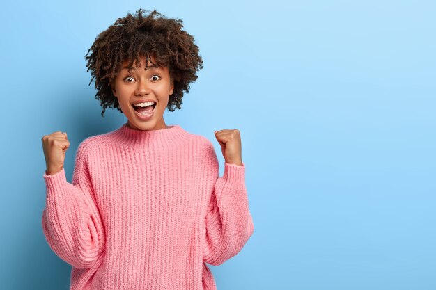 Mujer alegre con un afro posando en un suéter rosa