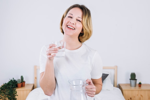 Mujer alegre con agua en el dormitorio