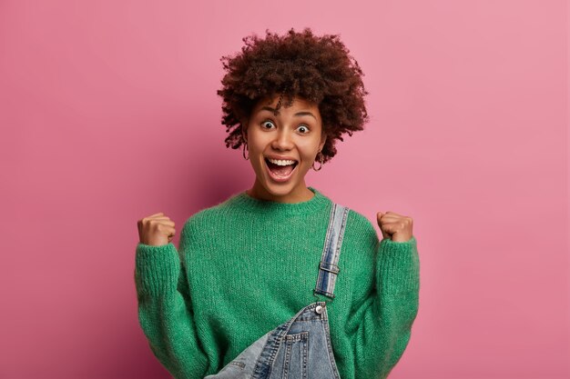 Mujer alegre y animada con cabello afro hace un puño y celebra la victoria