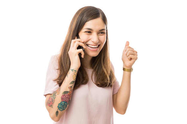 Mujer alegre apretando el puño mientras habla por teléfono móvil contra el fondo blanco.