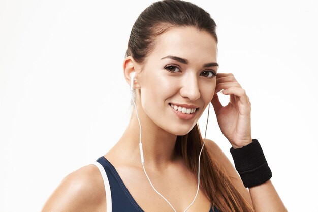 Mujer alegre de la aptitud deportiva en auriculares que sonríe en blanco.