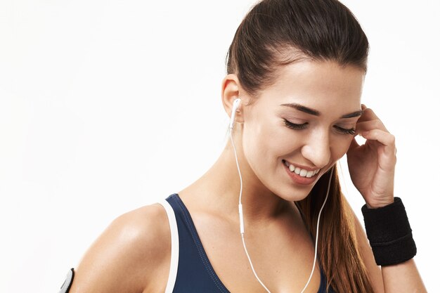 Mujer alegre de la aptitud deportiva en auriculares que sonríe mirando abajo en blanco.