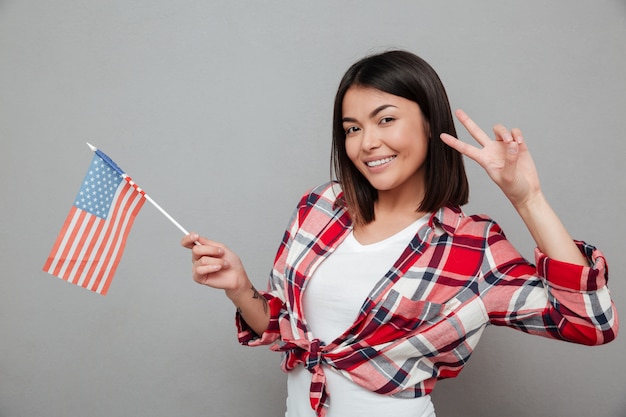 Mujer alegre con bandera de Estados Unidos sobre pared gris